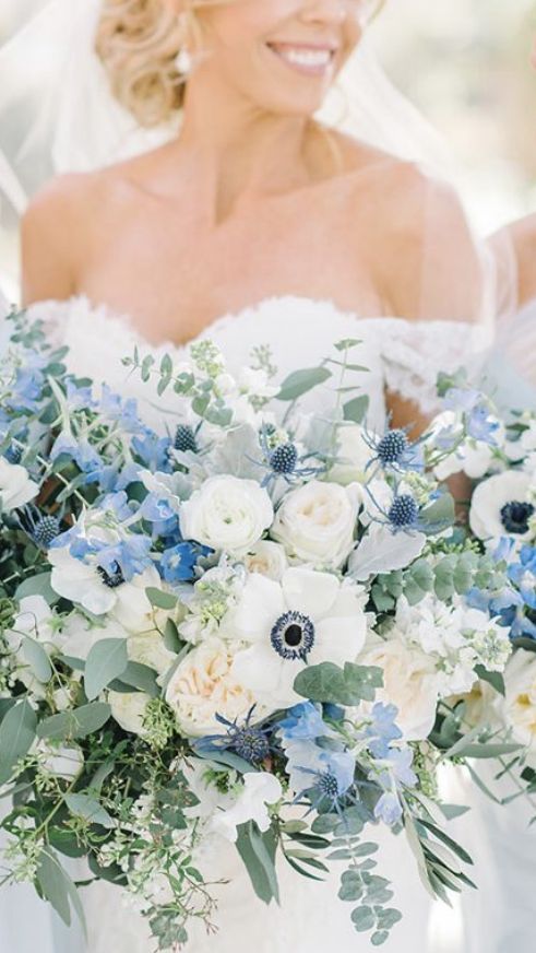 a lush wedding bouquet of white roses and anemones, some blue touches and thistles and lots of greenery just wows