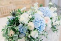 a lush wedding centerpiece of blue and white hydrangeas, blush roses, greenery and thistles is a cool and stylish solution