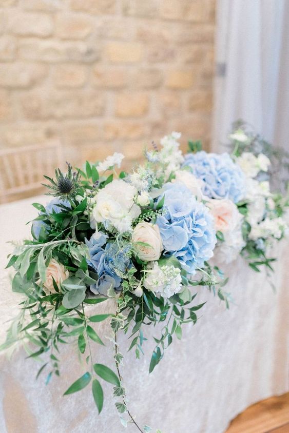 a lush wedding centerpiece of blue and white hydrangeas, blush roses, greenery and thistles is a cool and stylish solution