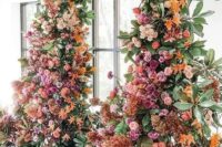 a luxurious colorful wedding arch decorated with greenery, blush, hot pink, orange and rust-colored blooms is wow
