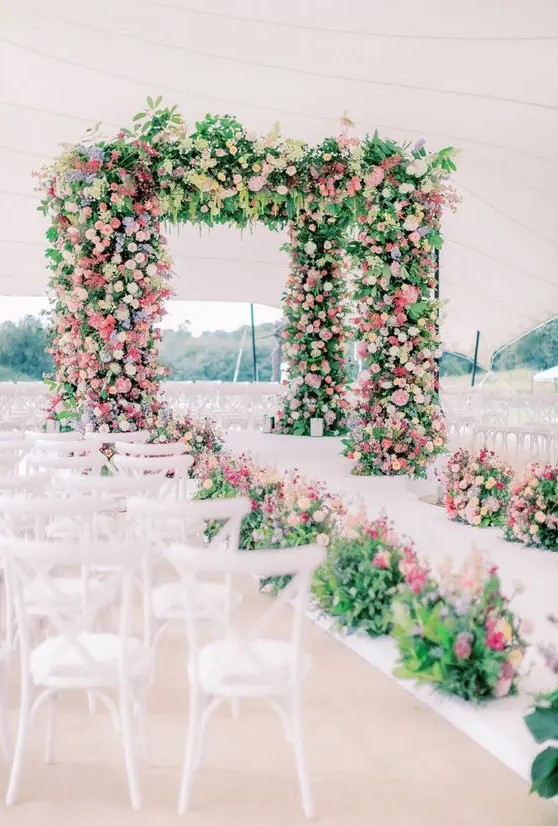 a massive wedding arbor covered with greenery, pink, lilac, blush and white blooms plus a matching wedding aisle