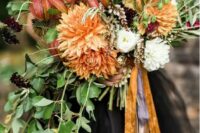 a moody Halloween wedding bouquet with orange blooms, dark purple flowers and cascading greenery