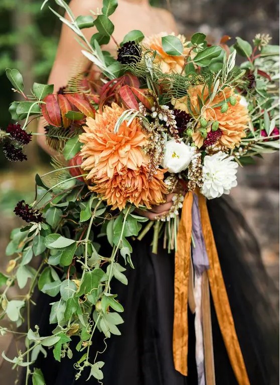 a moody Halloween wedding bouquet with orange blooms, dark purple flowers and cascading greenery