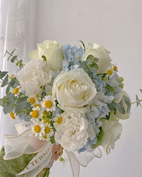 a neutral wedding bouquet of blue hydrangeas, white roses and carnations, chamolies, eucalyptus and some neutral ribbons
