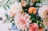 a pastel and muted color wedding centerpiece of blush and peachy dahlias, blue blooms and neutral roses and greenery for a spring celebration