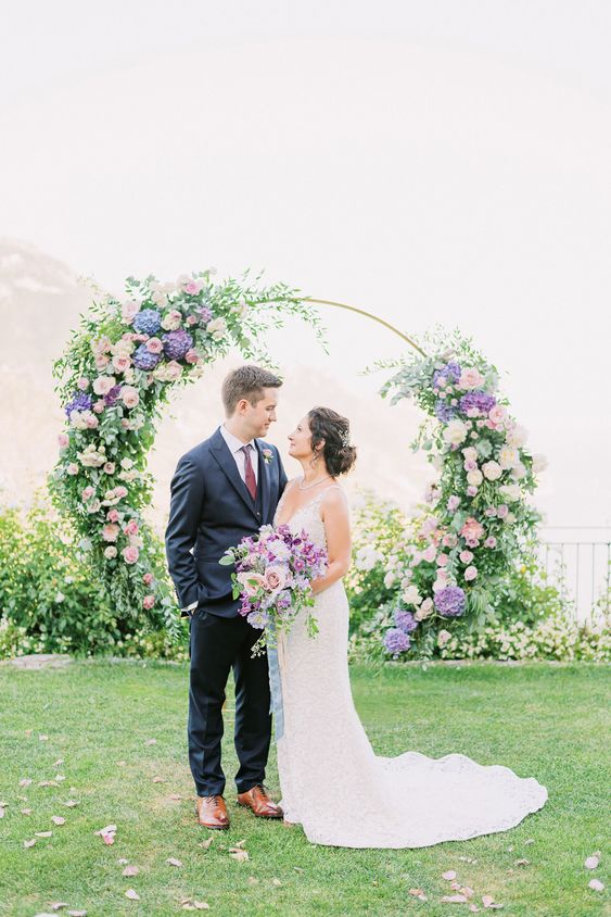 a pastel wedding arch decorated with greenery, blush roses, purple hydrangeas is a cool idea for a garden wedding