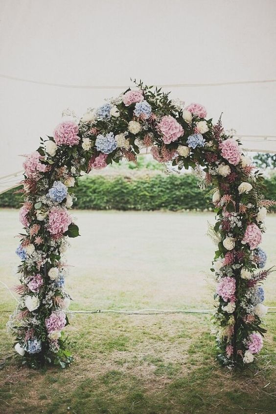 A pastel wedding arch with plenty of foliage and greenery, white, pink, blue hydrangeas is a cool and budget friendly solution