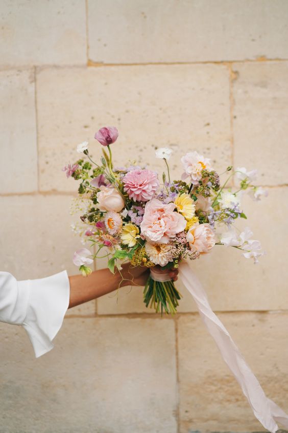 a pastel wedding bouquet of blush roses and carnations, sweet peas and other blooms, greenery and ribbons is wow