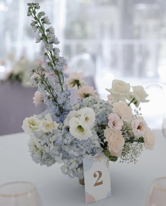 a pastel wedding centerpiece of blue hdyrangeas, blush and white blooms and blooming branches is a lovely solution