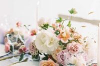 a pastel wedding centerpiece of blush and white roses and pink carnations, greenery and grasses plus candles