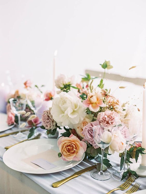 a pastel wedding centerpiece of blush and white roses and pink carnations, greenery and grasses plus candles
