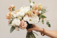 a peachy wedding bouquet of white ranunculus, blush and peachy roses and some greenery is amazing for spring or summer