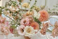 a pretty and chic textural and dimensional wedding centerpiece of orange dahlias, pink, neutral and light yellow blooms and greenery is wow