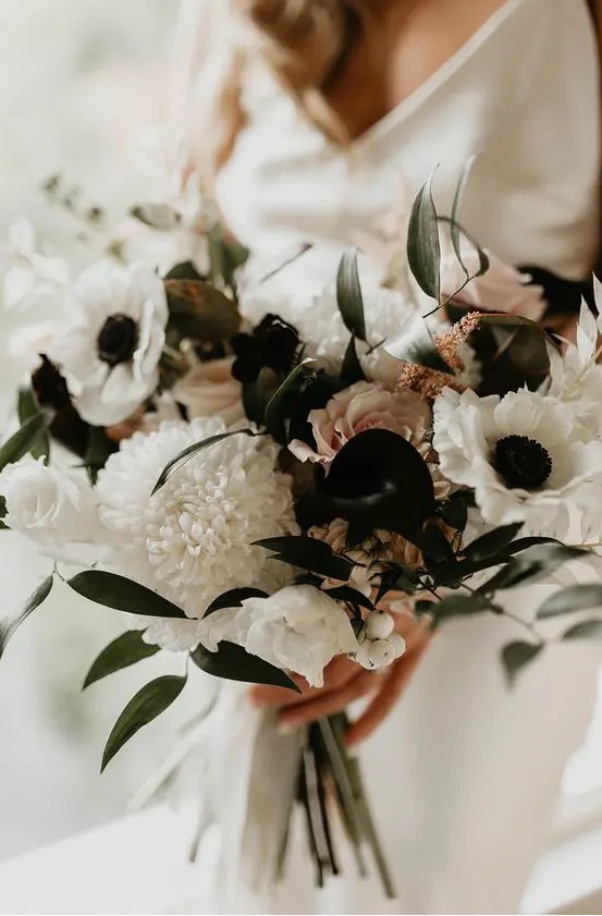 a pretty dimensional wedding bouquet of white roses, anemones, black callas and some blush roses and leaves is wow