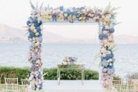 a pretty pastel wedding arch with white, blush and blue hydrangeas, deliphinium plus a cool sea view