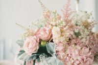 a pretty pink wedding centerpiece of roses, hydrangeas and astilbe, with pale miller and candles around is a lovely and chic idea