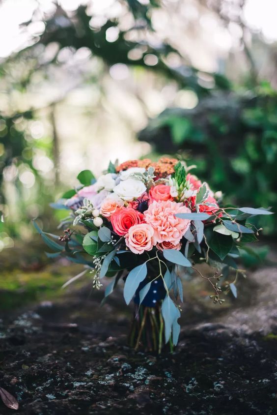 a pretty wedding bouquet of coral and pink roses and pink carnations, greenery and a wrap is a stylish and cool idea for summer
