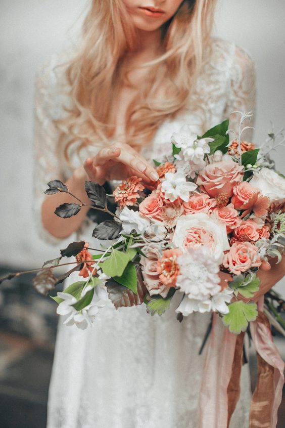 a pretty wedding bouquet of peachy and pink roses, white carnations, usual and dark foliage and some berries for a summer bride
