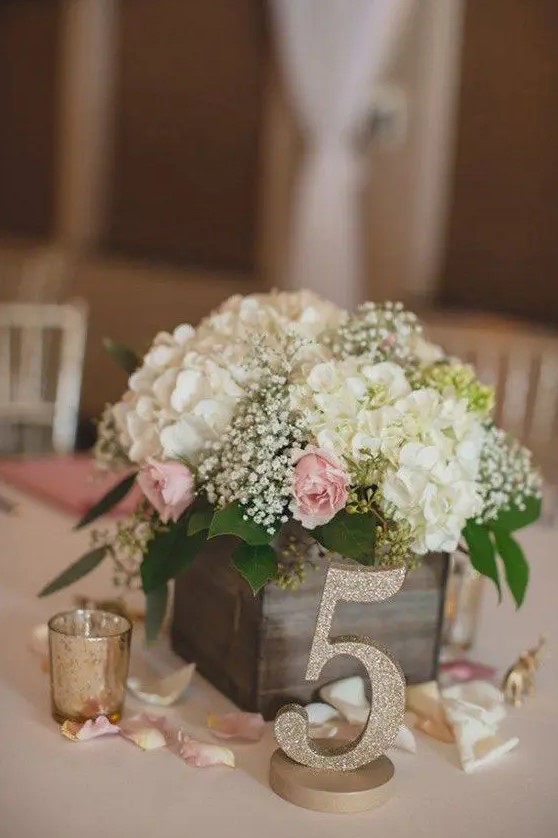 a reclaimed wooden box with baby's breath, hydrangeas and roses, a glitter table number for a rustic wedding centerpiece
