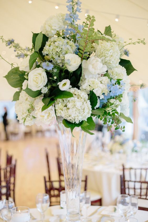a refined tall wedding centerpiece of white hydrangeas and roses, greenery and blue fillers for a spring or summer wedding