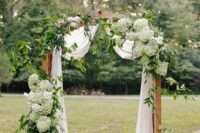 a refined wedding arch decorated with greeneyr and white and green hydrangeas and some white fabric is an elegant and stylish idea