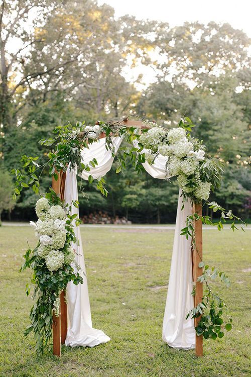 a refined wedding arch decorated with greeneyr and white and green hydrangeas and some white fabric is an elegant and stylish idea