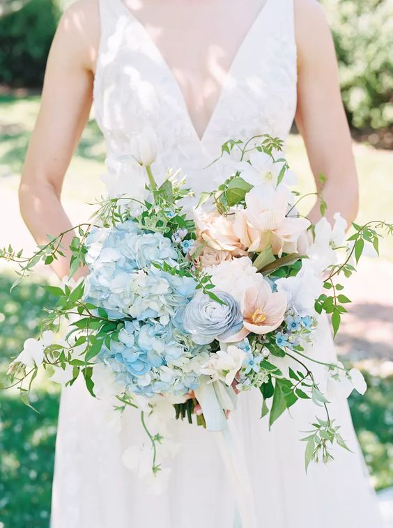 a refined wedding bouquet of blue hydrangeas, peachy and blush blooms, greenery and twigs is a lovely idea for spring