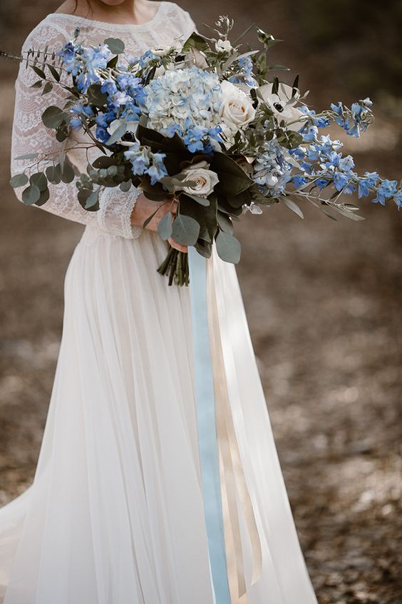 a romantic dimensional wedding bouquet of white roses and blue hydrangeas plus other blooms, foliage and greenery
