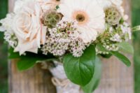a romantic wedding bouquet of blush roses and gerberas, seed pods, waxflowers and leaves, with a burlap and lace wrap