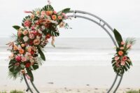 a round tropical wedding arch with pink, hot pink, orange blooms and fronds and leaves for a tropical wedding