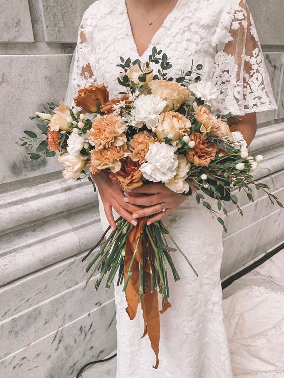 a rust-colored dimensional wedding bouquet of white and rust carnations, berries, greenery and rust-colored ribbons is wow