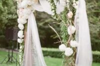 a rustic wedding arch done with greenery, white and blush hydrageas and roses, twigs and sheer tulle is cool