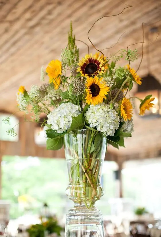 a rustic wedding centerpiece of white hydrangeas, sunflowers, wildflowers and foliage is a lovely idea for a laid-back summer wedding