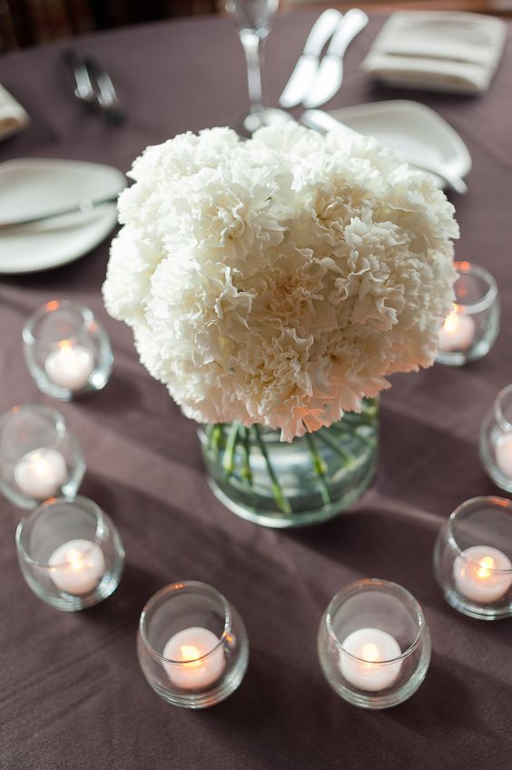 a simple and classic white carnation wedding centerpiece surrounded with candles is a lovely idea for a modern wedding