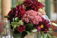 a simple and cute rustic fall wedding centerpiece of a tree stump, burgundy blooms of various kinds and greenery is a lush and beautiful idea