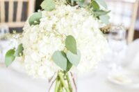 a simple and stylish white hydrangea wedding centerpiece with greenery and candles around is a cool and lovely idea