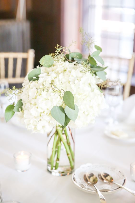 a simple and stylish white hydrangea wedding centerpiece with greenery and candles around is a cool and lovely idea