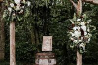 a simple rustic wedding arch with a curved top, of logs, white and burgundy blooms and greenery and white pumpkins on the ground