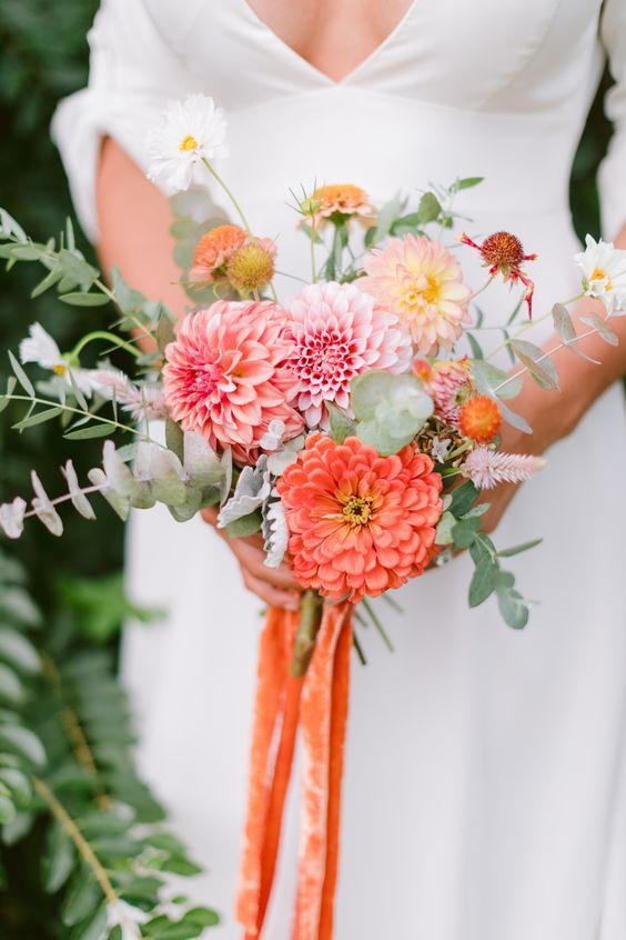 a small and colorful wedding bouquet of pink, blush and orange dahlias, some white and orange fillers, greenery and ribbons