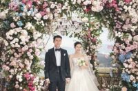 a statement floral wedding arch decorated with greenery, blush, blue and fuchsia blooms and blooming branches for a bold wedding