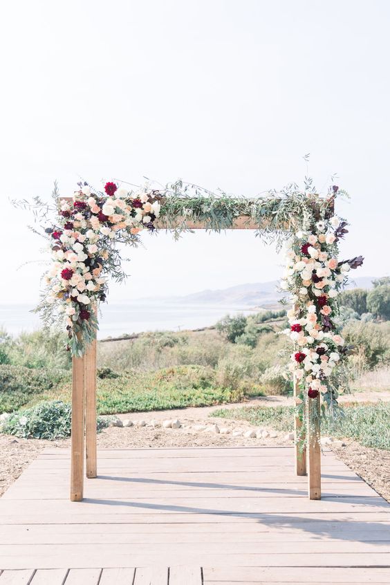 a stylish and contrasting boho wedding arch decorated with greenery, white, blush and burgundy dahlias is a lovely idea for the fall