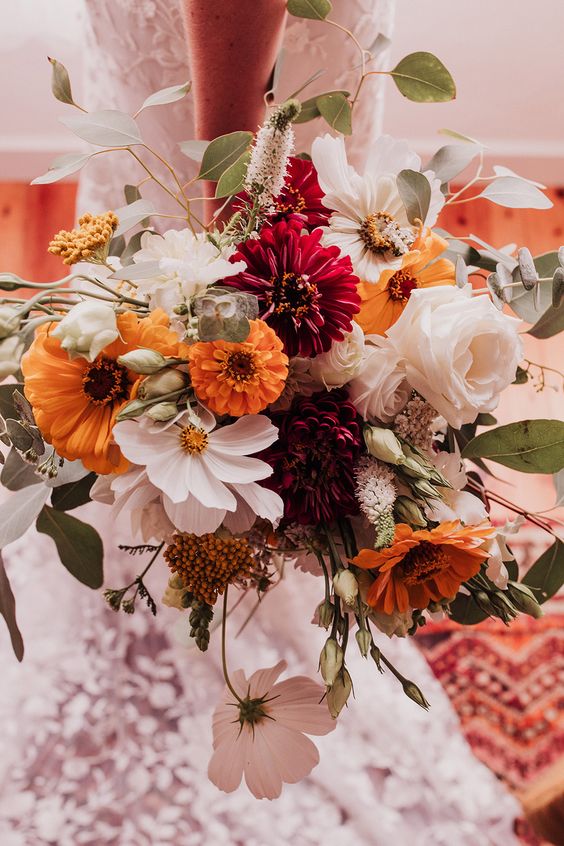 a stylish fall wedding bouquet of white roses and daisies, burgundy and orange dahlias and gerberas, some greenery