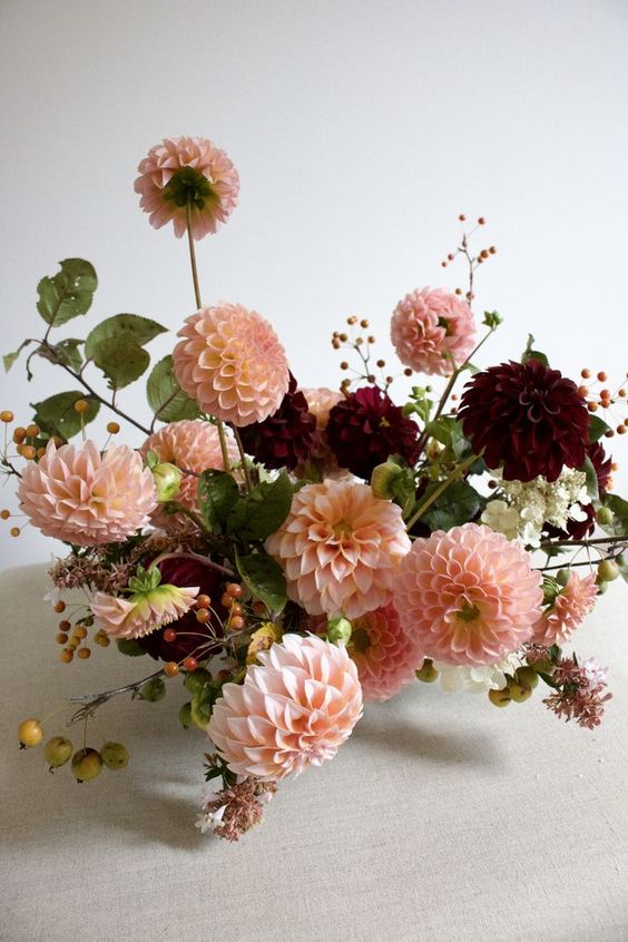 a stylish fall wedding centerpiece of burgundy and blush dahlias, berries and greenery is a cool and contrasting arrangement