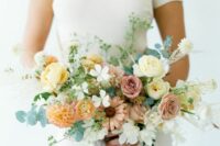 a stylish modern wedding bouquet of yellow, mauve and orange blooms including roses, ranunculus and dahlias and greenery