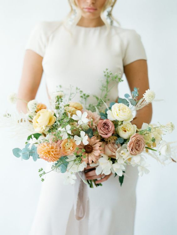 a stylish modern wedding bouquet of yellow, mauve and orange blooms including roses, ranunculus and dahlias and greenery