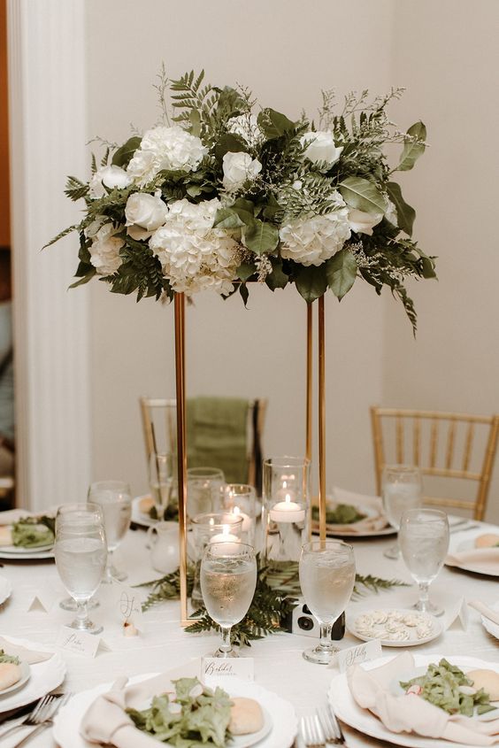a stylish tall wedding centerpiece of white roses and hydrangeas, greenery and floating candles is a lovely idea for a spring or summer wedding