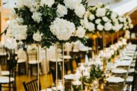 a stylish tall wedding centerpiece of white roses, hydrangeas and greenery, a greenery runner on the table and floating candles