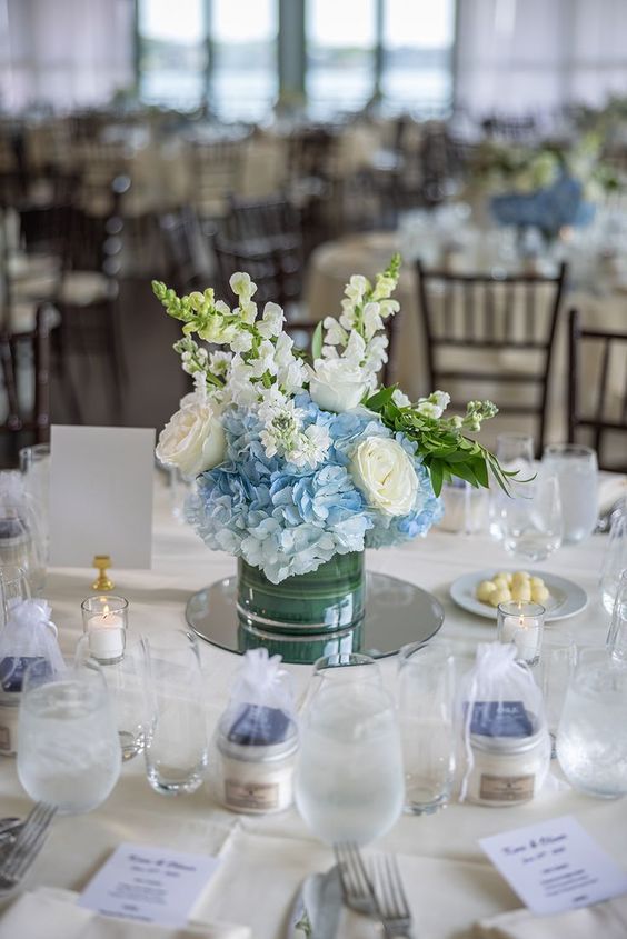 a stylish wedding centerpiece of blue hydrangeas and white roses and greenery is a classyc idea for a rustic or coastal wedding