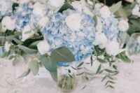 a stylish wedding centerpiece of blue hydrangeas and white roses plus greenery is great for a blue-infused wedding