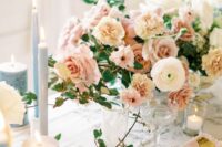 a subtle and delicate wedding centerpiece of blush roses and carnations, white ranunculus and greenery plus candles around is wow